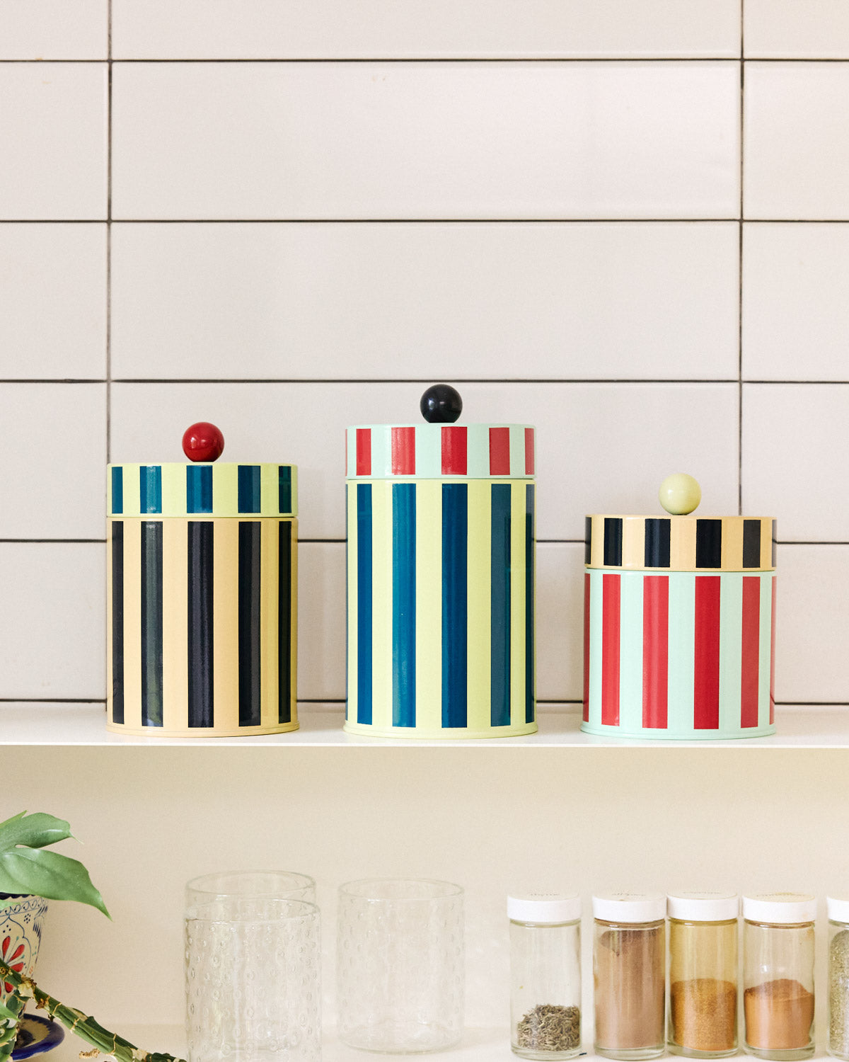 Colorful striped canisters on a shelf against a tiled wall.