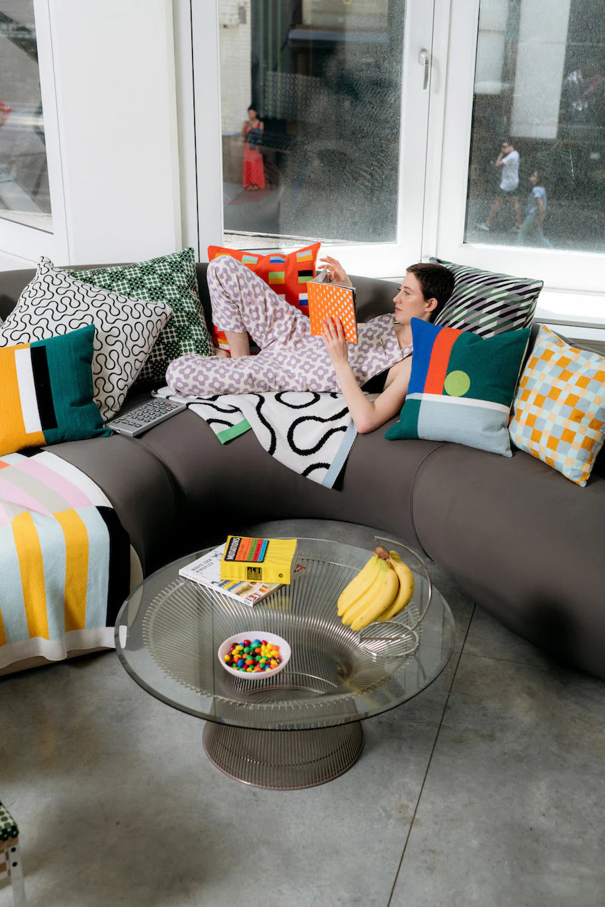Woman sitting on a modern sofa with colorful cushions in a room with large windows.