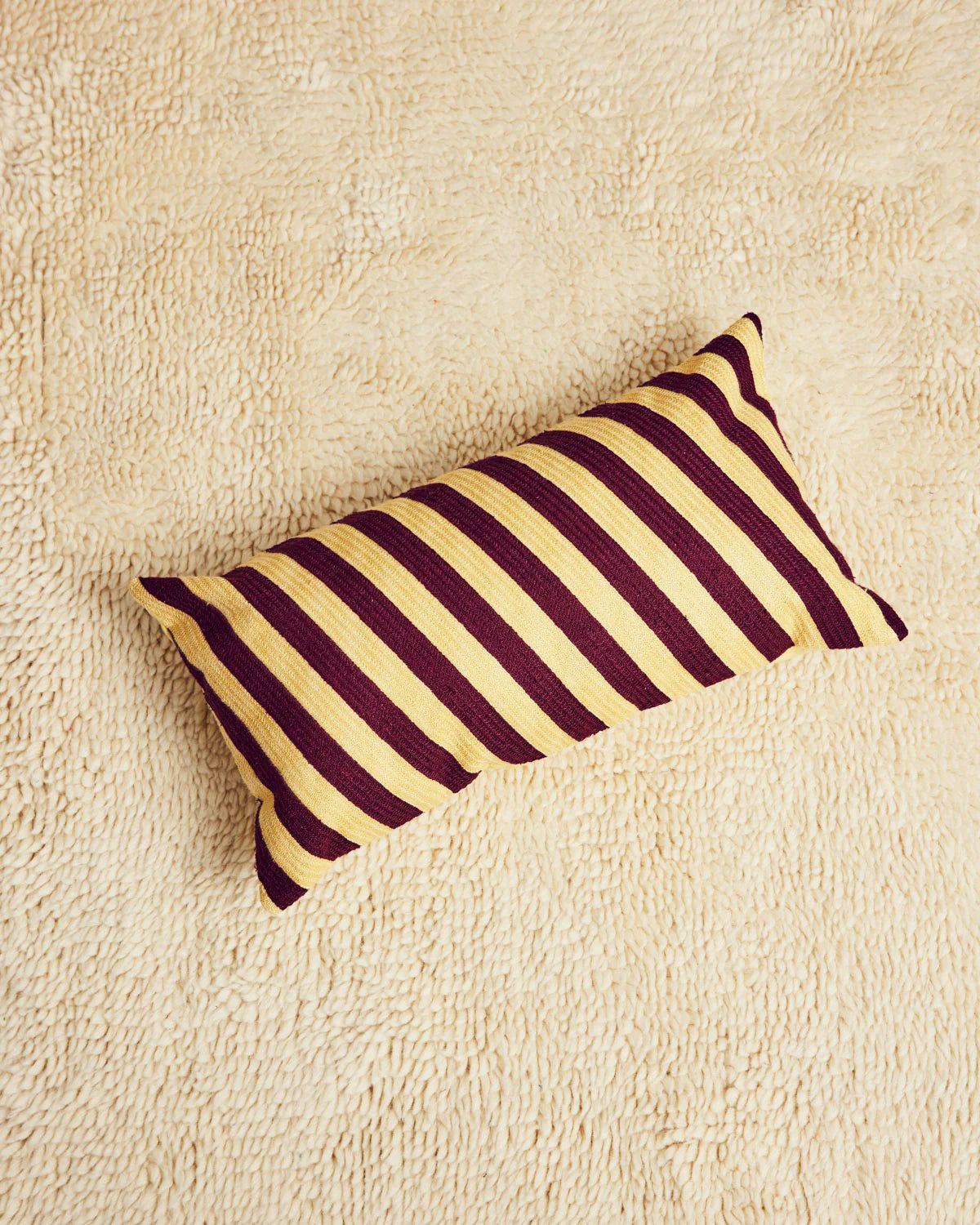 Striped pillow with purple and yellow pattern on a beige surface